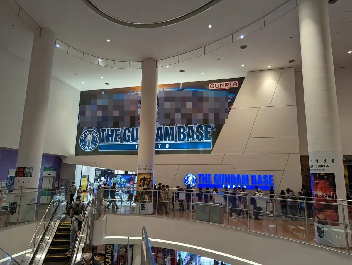 Entrance of THE GUNDAM BASE TOKYO inside DiverCity Tokyo Plaza, with the store sign on the wall and visitors queuing behind rope barriers
