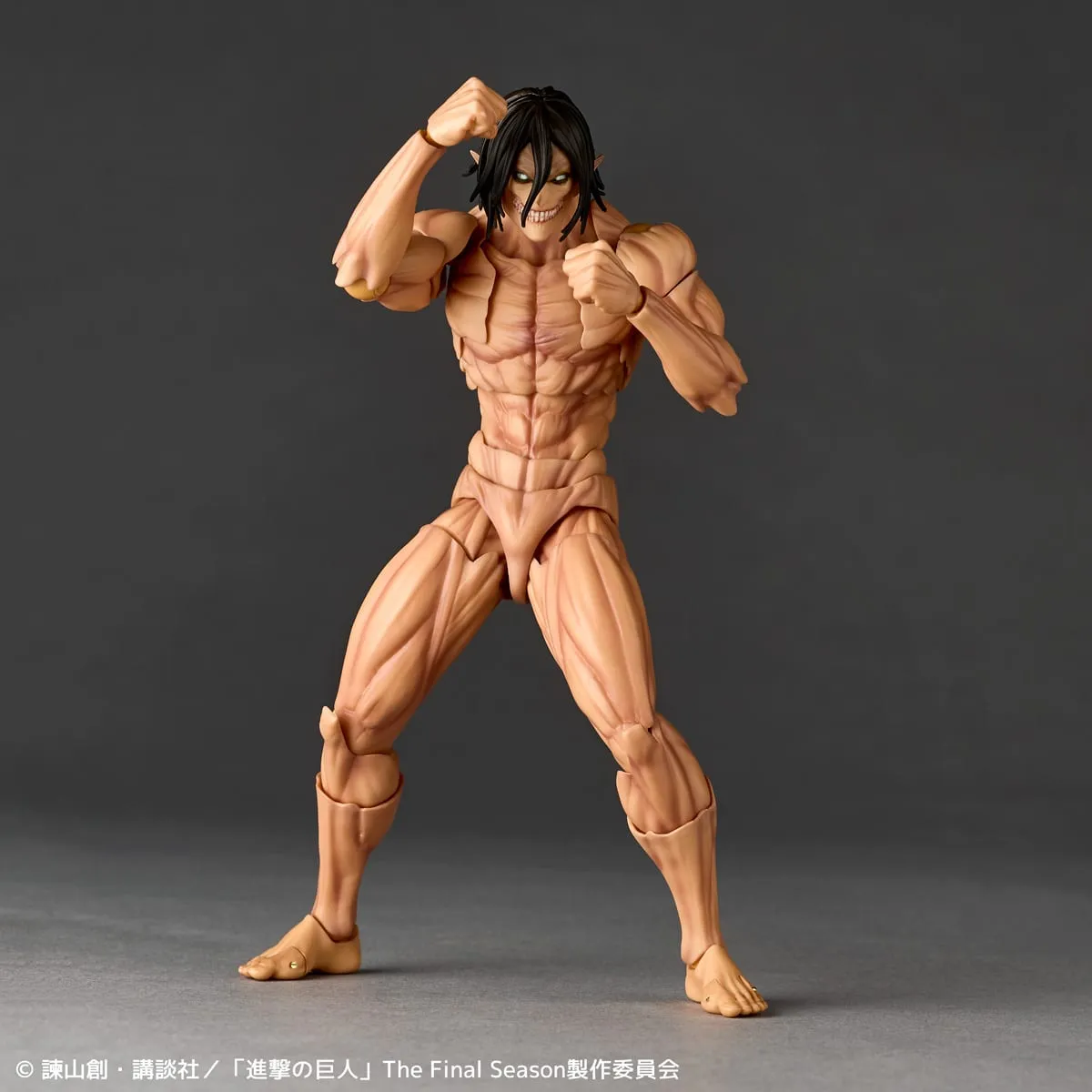 Revoltech Amazing Yamaguchi Attack Titan action figure from Attack on Titan, Eren Yeager's muscular titan form with black hair and bared teeth, standing in a wide fighting stance with one fist raised and the other at chest height on a dark gray background, official Kaiyodo sample photo
